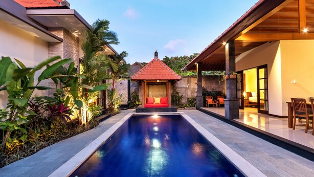 A swimming pool with a red-roofed structure in the background, surrounded by lush greenery.