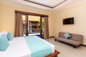 A hotel room with a bed, a sofa, a TV, and a view of an outdoor area with a pool and dining area.