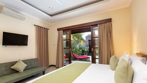 A hotel room with a bed, a sofa, a TV, and a view of a pool and palm trees.
