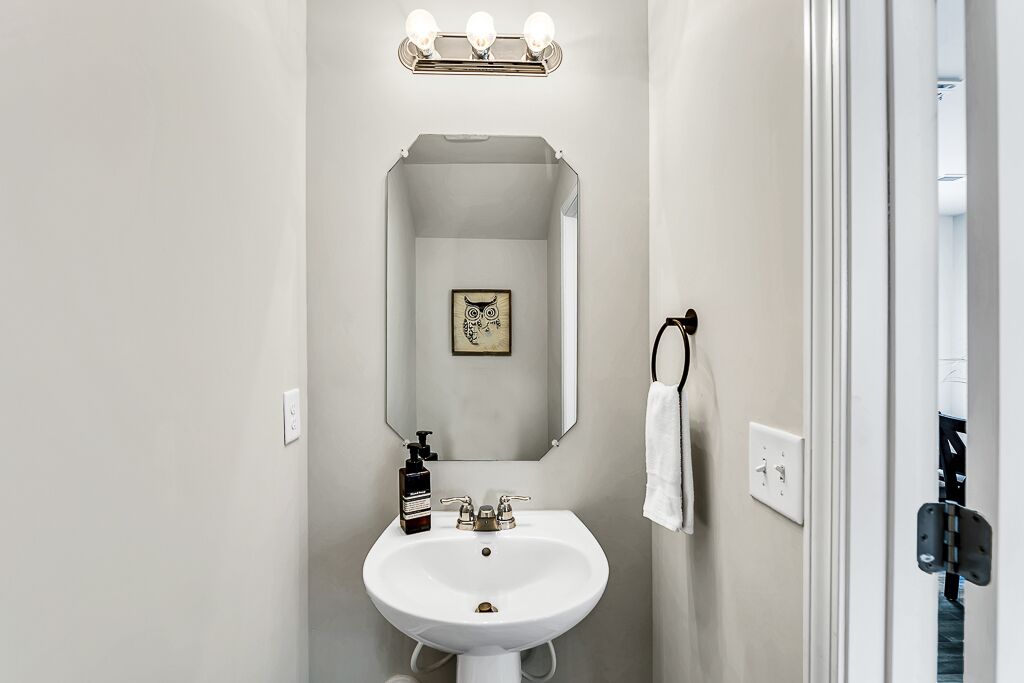 A bathroom with a white sink, a mirror, and a light fixture above the mirror.