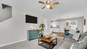 A living room with a sofa, coffee table, and a television. There is a kitchen in the background. - Sleeps 6 - 3 Queen Beds - 2 Mi Wake Forest + Hospital (Winston-Salem)