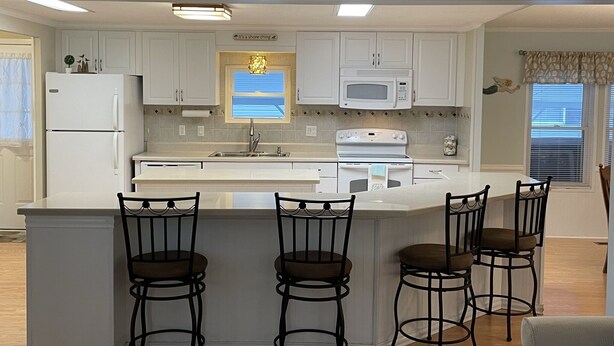 A modern kitchen with white cabinets, a central island with bar stools, a refrigerator, a microwave, and an oven. - 3 bedroom house that sleeps 9 located in Oceanside Village, Surfside Beach (Surfside Beach)
