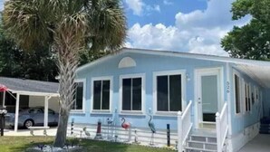 A light blue building with a covered porch, a palm tree, and a statue of a flamingo. - 3 bedroom house that sleeps 9 located in Oceanside Village, Surfside Beach (Surfside Beach)
