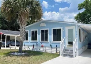 A light blue building with a covered porch, a palm tree, and a flamingo statue.
