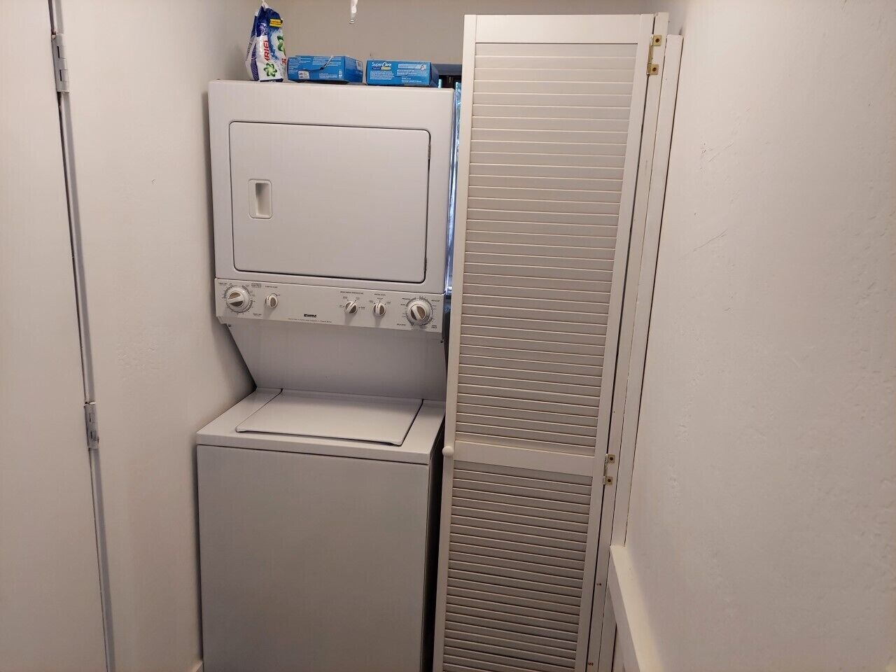 Une petite buanderie comprenant un lave-linge et un sèche-linge, un petit meuble de rangement et une porte en métal.