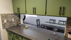 A kitchen with green cabinets, a countertop, and a dining area with a table and chairs. - Camelia's cabin (Pinetop)