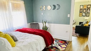 A bedroom with a bed, a colorful rug, a wall with moon phases, and a hallway leading to another room.