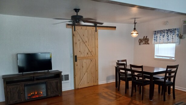 Una sala de estar con televisor, chimenea, mesa de comedor, sillas y ventilador de techo.