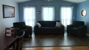 Una sala de estar con un sofá marrón oscuro, dos sillones, una mesa de centro de madera y un cuadro en la pared.
