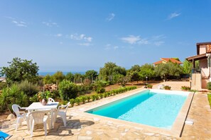 A swimming pool with a patio area, surrounded by greenery and a view of the sea. - Villa Milizie, Scicli, Italy (Scicli)
