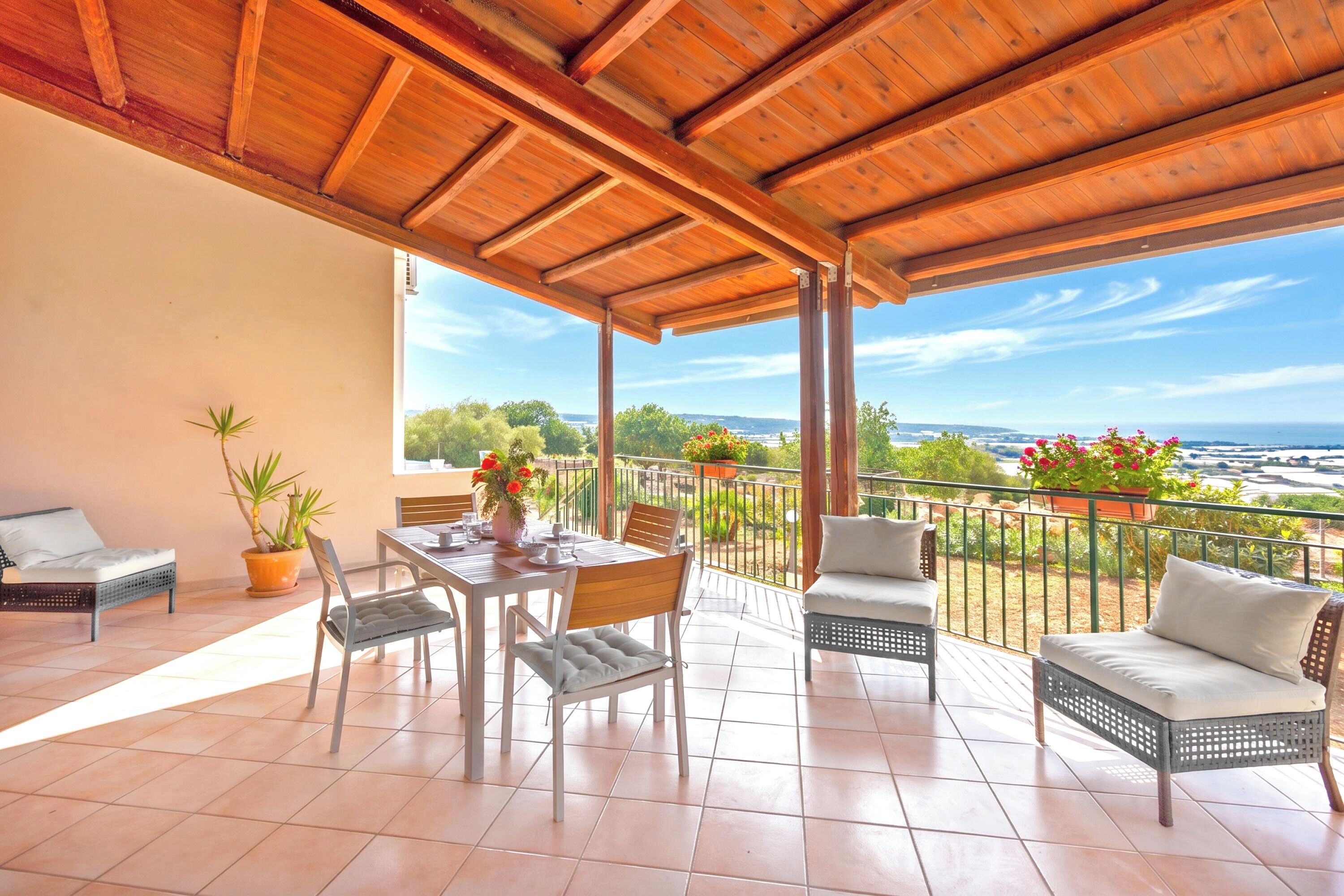 A covered outdoor patio with a table and chairs, a sofa, and potted plants.