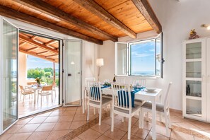 A dining area with a table set for four, a view of the outdoors, and a white cabinet with glass doors. - Villa Milizie, Scicli, Italy (Scicli)