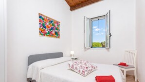 A bedroom with a bed, a nightstand, a chair, a window, and a colorful wall decoration.