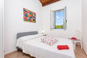 A bedroom with a bed, a nightstand, a chair, a window, and a colorful wall decoration. - Villa Milizie, Scicli, Italy (Scicli)