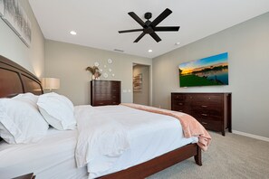 Ein Schlafzimmer mit Bett, Deckenventilator, Gemälde und Kommode.