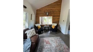 Una sala de estar acogedora con un sofá marrón, dos sillones, una mesita de centro y un ventanal con techo de madera.