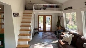 Un salón espacioso con una escalera que sube a un altillo, un ventanal grande y un sofá de cuero.
