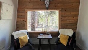 Una habitación acogedora con techo inclinado, paneles de madera, un ventanal grande y dos sillones con cojines.