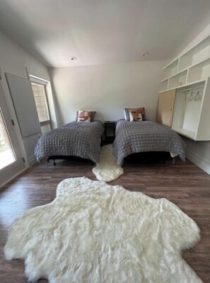 Une chambre avec deux lits, un tapis en fausse fourrure blanche, un plancher en bois et une armoire blanche.