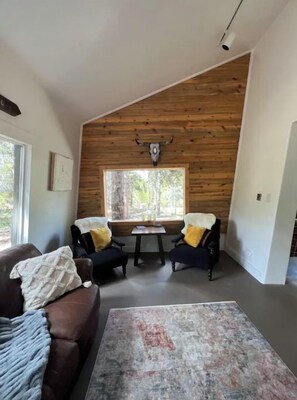 Una sala de estar acogedora con un sofá marrón, dos sillones, una mesita de centro y un ventanal con techo de madera.