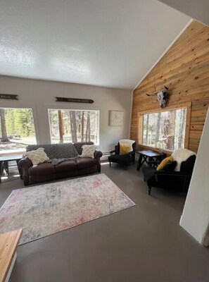 Relax in this cozy living area with a high ceiling, leather sofa, and a view of the surrounding forest.