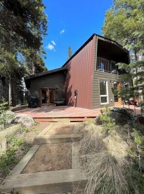 Une cabane moderne à deux étages, dotée d’une terrasse en bois et d’une grande fenêtre à l’étage supérieur.