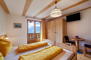 A room with two beds, a wooden wardrobe, a television, and a balcony with a mountain view.