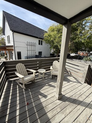 Une terrasse en bois, agrémentée de chaises Adirondack et d’une petite table, d’où l’on peut admirer un bâtiment blanc coiffé d’un toit noir.