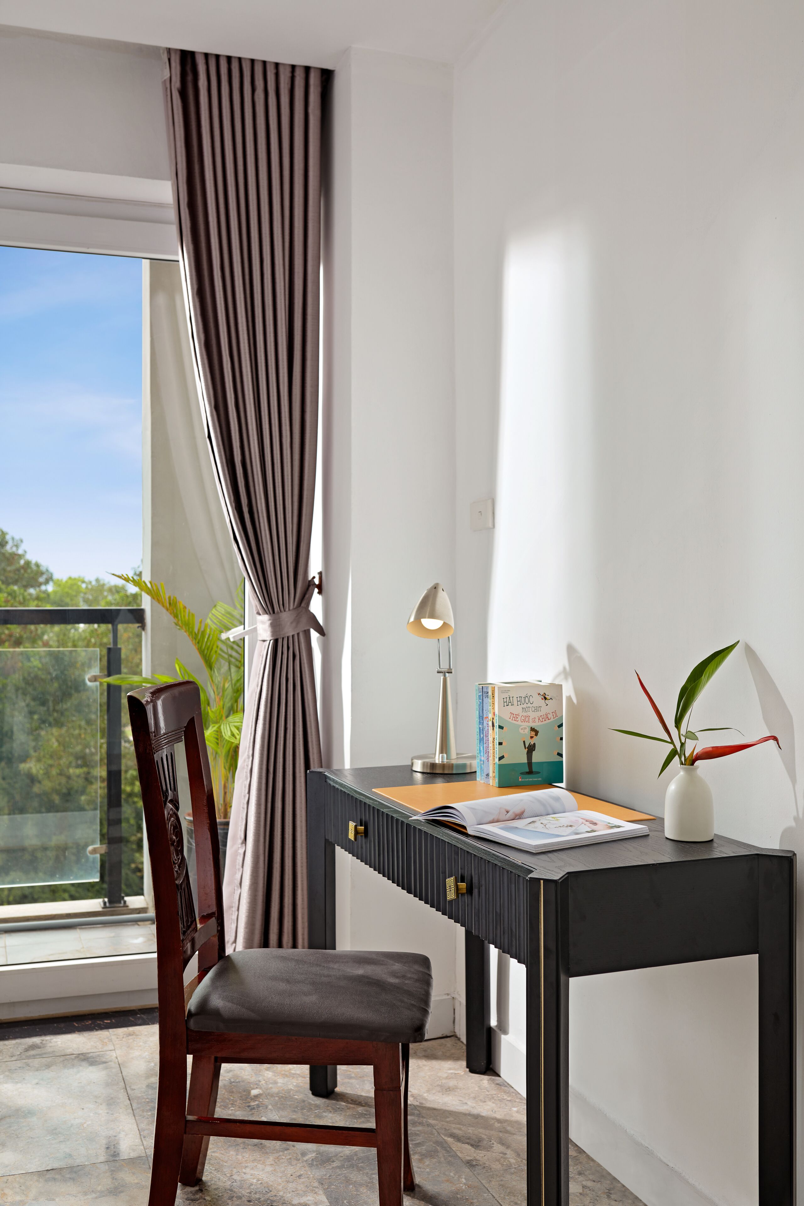 A modern room with a wooden chair, a desk with a lamp, a book, and a plant.