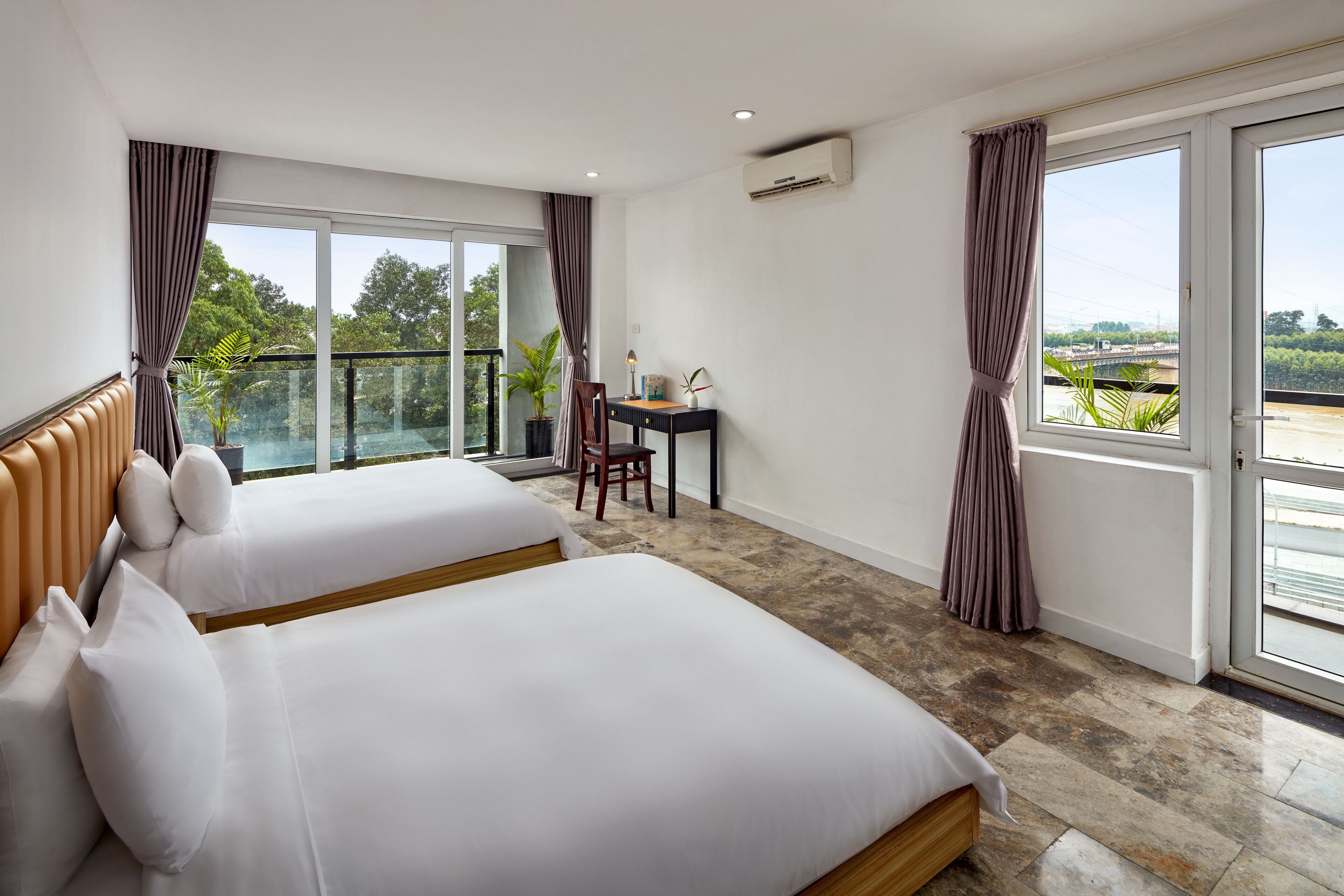 Quarto de hotel com duas camas, uma escrivaninha e varanda com vista para o verde.