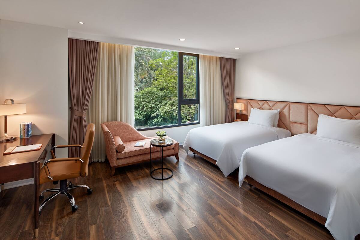 A hotel room with two beds, a desk, a chair, and a window with curtains.