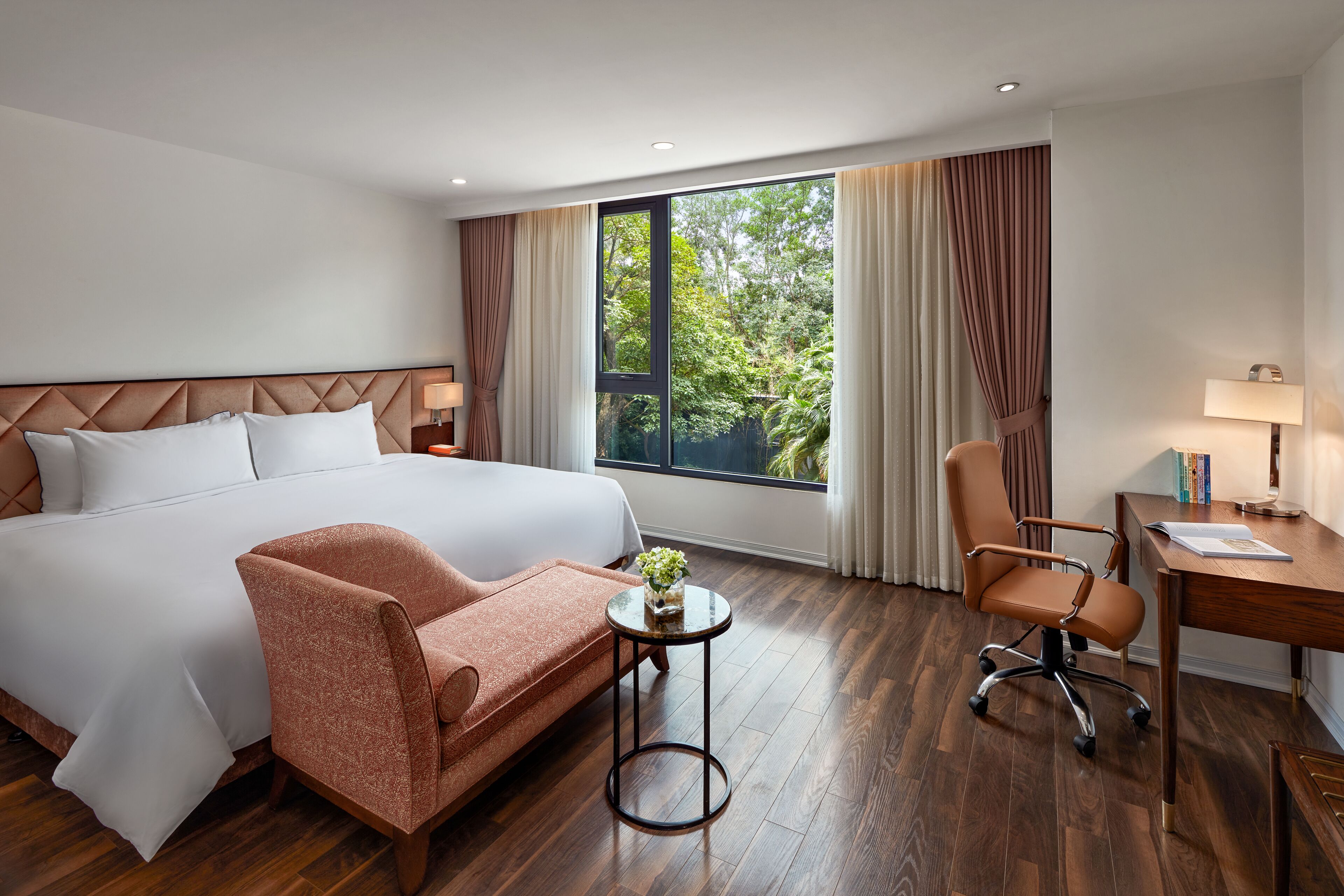 A hotel room with a large bed, a desk, a chair, and a small table with a plant.