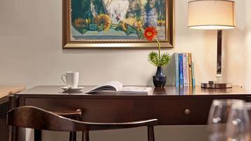 Une pièce comprenant un bureau, une chaise et une table avec un verre à vin. Il y a un tableau au mur et une lampe sur le bureau.