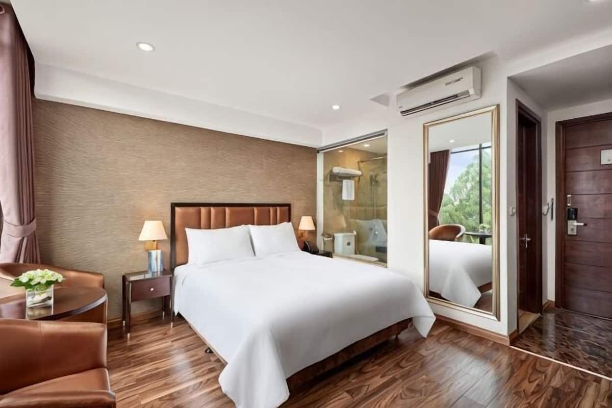 A hotel room with a bed, a nightstand, a chair, a mirror, and a door.