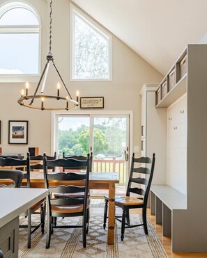 Un coin repas agrémenté d’un lustre, de chaises en bois, d’une table et d’une vue sur l’extérieur, visible à travers une porte vitrée.