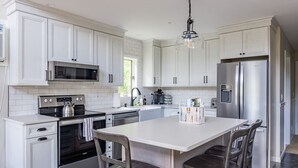 Una cocina moderna con armarios blancos, electrodomésticos de acero inoxidable y una isla central con sillas.