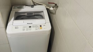 Une petite machine à laver blanche, placée dans un coin d’une pièce dont les murs sont recouverts de carreaux et qui est équipée d’une main courante en métal.