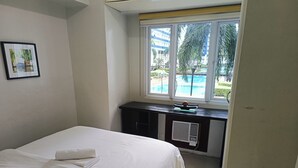 Une chambre d’hôtel avec un lit, un bureau équipé d’un ordinateur et une fenêtre donnant sur une piscine et des immeubles.