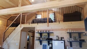 A wooden interior with a bunk bed, a staircase, and kitchen shelves with various items. - Magical Off grid Lakefront Cabin (Lone Butte)