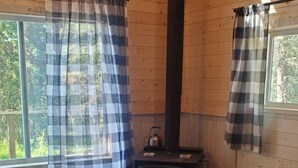 A cozy cabin interior with a wooden floor, a sofa, a table, and a wood-burning stove. - Magical Off grid Lakefront Cabin (Lone Butte)