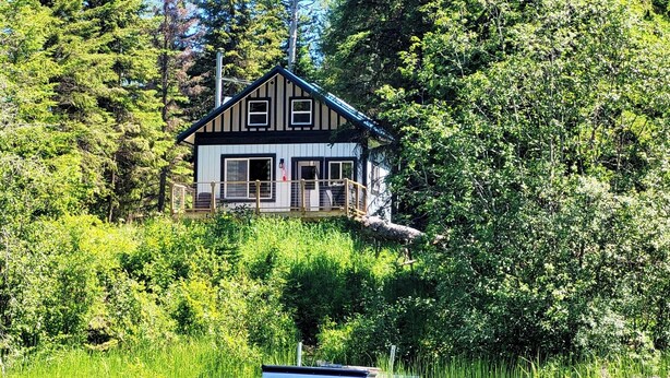 A cabin with a dock extending into a lake, surrounded by dense greenery. - Magical Off grid Lakefront Cabin (Lone Butte)
