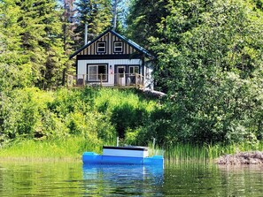 Une cabane avec un quai s’avançant dans un lac, entourée d’une végétation luxuriante.