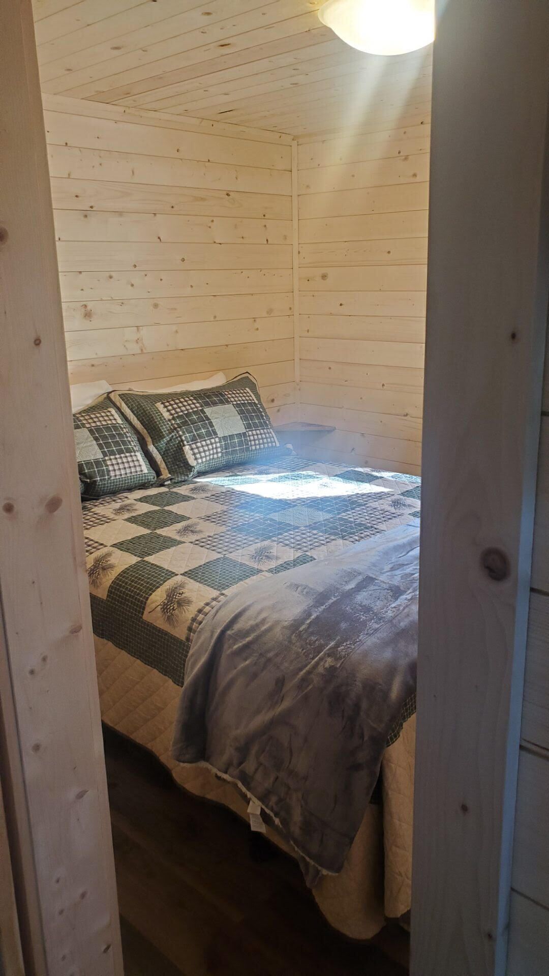 A wooden cabin room with a bed, a quilt, and a window.