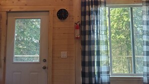 A wooden cabin interior with two windows, a door, a clock, and a fire extinguisher. - Magical Off grid Lakefront Cabin (Lone Butte)