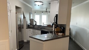 Une cuisine moderne avec des meubles blancs, un îlot central et un coin repas comprenant une chaise et une table blanches.