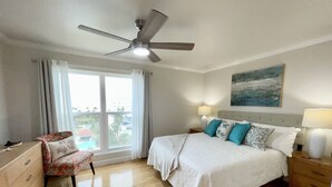 Une chambre d’hôtel avec un lit, une chaise, une table de chevet, un ventilateur de plafond et une fenêtre avec des rideaux.
