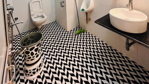 A bathroom with a black and white patterned floor, a white sink, a mirror with a geometric pattern, and a toilet with a bidet attachment. - Hotel Buddha Park (Varanasi)