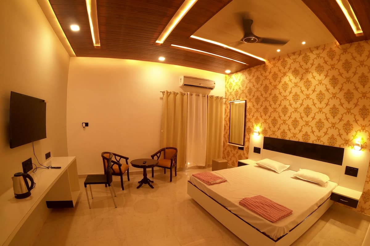 A hotel room with a bed, a desk with a chair, a television, an air conditioning unit, and a ceiling fan.