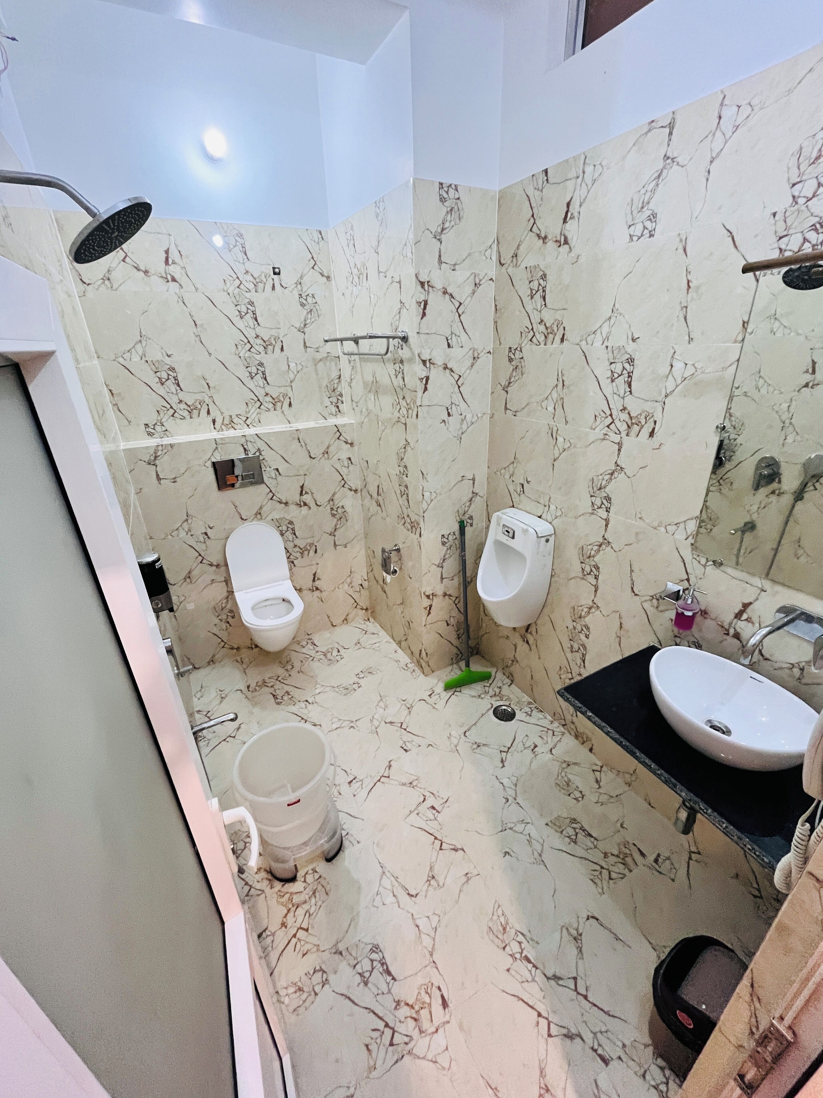 Un bagno con pavimento in marmo, un lavandino, uno specchio, una doccia e due orinatoi.