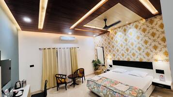 A hotel room with a bed, a desk with a chair, a ceiling fan, and a patterned wallpaper.